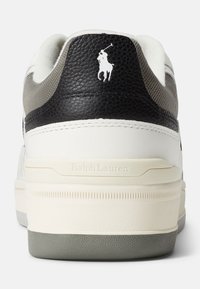 Zapatilla de cuero blanca con acentos en negro y gris. Presenta un logo en relieve, materiales texturizados y una suela de goma con estrías horizontales.