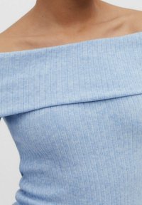 Helles blaues, geripptes Off-Shoulder-Oberteil mit gefaltetem Kragen und figurbetontem Design. Weiche Textur und minimalistischer Stil.
