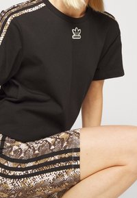 Svart bomulls-T-shirt med Adidas-logga vid halsen, kombinerad med ormskinnsmönstrade shorts med svarta ränder och kontrasterande färger.