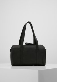 Czarna skórzana torba z dwoma krótkimi uchwytami, cylindryczny kształt, gładka faktura i subtelne detale przeszycia. Posiada odpinany pasek.