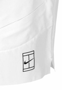 Camicetta bianca con il logo Nike in nero, caratterizzata da un design geometrico distintivo. Include una tasca laterale e una texture liscia.