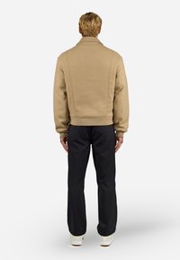Beige svršek z vlněnou směsí se strukturovaným límcem, ribbed spodním lemem a manžetami. Černé kalhoty s uvolněným střihem a širokými nohavicemi, nošené se světlými botami.