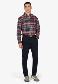 Camisa de cuadros en tonos burdeos, azul marino y verde, combinada con pantalones azul marino oscuros y zapatillas grises. Presenta un cinturón marrón con herrajes plateados.
