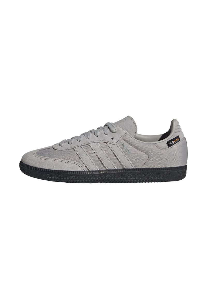 Zapatillas de ante gris con suela de goma negra, que presenta un diseño de tres rayas, puntera redonda y cierre de cordones. Incluye un acento de marca en el talón.