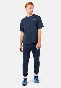 Námořnická bavlněná tričko s uvolněným střihem, doplněné o odpovídající tepláky. Obsahuje žebrované manžety a modré sportovní boty s černými akcenty na podrážce.