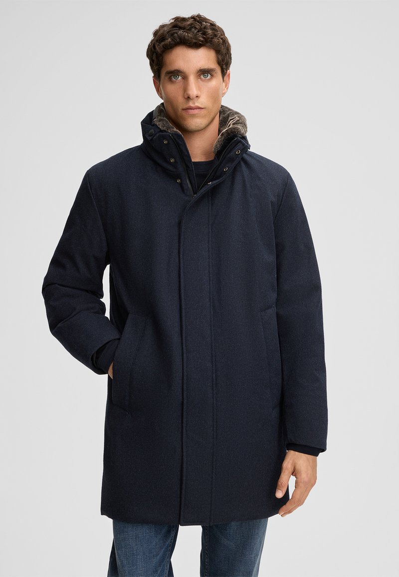 Cappotto blu navy con finitura testurizzata, cappuccio e tasche frontali. Presenta una chiusura a bottoni e un rivestimento interno in contrasto. Design elegante e su misura.