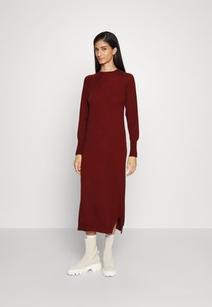 Vestido de malha longo em bordô, com decote redondo, punhos canelados e fendas laterais. Combinado com botas de tornozelo grossas em off-white. Textura suave.