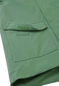 Giacca verde con tasca piegata con chiusura in Velcro, texture liscia e dettagli riflettenti sottili. Design semplice e funzionale.