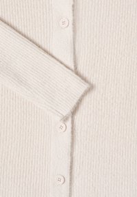 Strickjacke aus weichem, cremefarbenem Material mit vertikalen Rippungen, fünf runden Knöpfen und einem lässigen Ärmel.