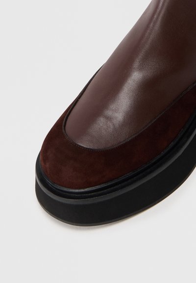 Bruine leren en suède schoen met een ronde neus, voorzien van een zwarte gestructureerde zool en contrasterende bovenmaterialen. Gladde en matte afwerking.
