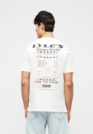 Noormees, kes kannab valget t-särki, millel on poodkviitungi graafiline trükk, kus on loetletud toiduained, hinnad ja tagaküljel fraas „Jäta vahe tagasi“.