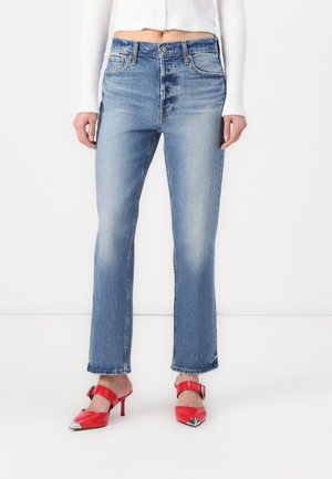 Light blue denim jeans with a straight leg design, mid-rise waist, and a faded pattern. Paired with red, pointed-toe heels.
