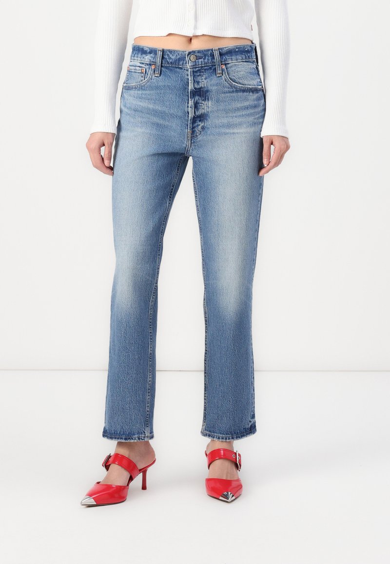 Lyseblå denimjeans med rett ben-design, midjehøyde og falmet mønster. Sammen med røde spisse hæler.