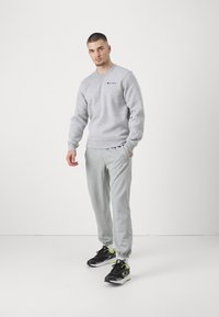 Felpa grigia con scollatura a girocollo e logo, abbinata a joggers grigi con tasche laterali. Scarpe nere con accenti neon.