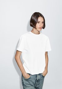 T-shirt bianco a maniche corte con scollatura rotonda, realizzato in un tessuto liscio, abbinato a jeans blu in denim larghi. Design semplice e pulito con dettagli minimi.