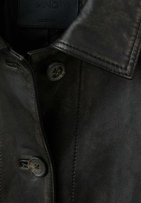 Gros plan d'une veste en cuir noire montrant le col, les boutons, les coutures et une étiquette indiquant MNG Leather.