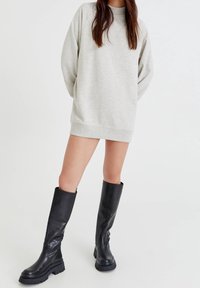 Robe sweatshirt grise à manches longues, associée à de hautes bottes en cuir noir avec une semelle épaisse et une texture lisse.