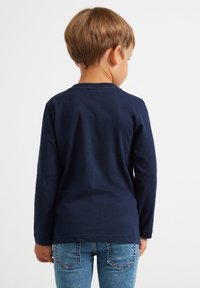 Langärmliges, navyblaues Hemd aus Baumwolle, mit rundem Halsausschnitt und glatter Textur, kombiniert mit hellblauen Jeans.