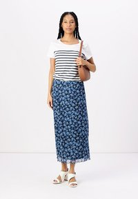 Pruhované bílé a námořnické tričko kombinované s dlouhou modrou květinovou sukní. Bílé klínové sandály. Hnědá crossbody taška. Hladká tkanina, volný střih.