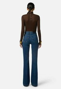 Top marrone a maniche lunghe con bottoni sul retro, abbinato a jeans blu a zampa d'elefante con tasche e design a vita alta.