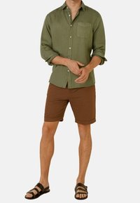 Helles grünes Kurzarm-Hemd mit Brusttasche, braune Shorts und schwarze Sandalen, mit einem lässigen Schnitt.