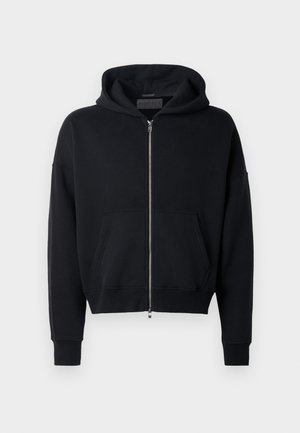 Crna zip-up dukserica napravljena od mekanog materijala s prednjim džepom, oversized kroj i zaobljenom kapuljačom. Ima rebraste manžete i donji rub.