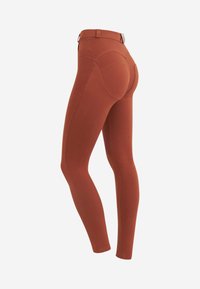 Leggings aderenti realizzati in un materiale elasticizzato, di colore arancione bruciato, con un elastico in vita e dettagli a cucitura curva sul retro.