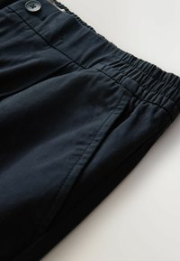 Pantaloni bleumarin cu un elastic la talie, având detalii cu nasturi, plisări și o textură de stofă netedă.