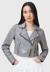 Giacca cropped in pelle grigia con colletto a punta, zip frontali e tasche con zip. Texture liscia e design aderente.