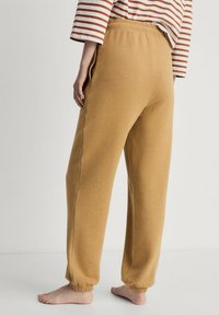 Bruine katoenen sweatpants met zijzakken, elastische tailleband en opgerolde enkels. De stof lijkt zacht en heeft een licht gestructureerde uitstraling.