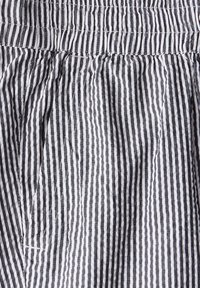 Tissu rayé noir et blanc avec une taille élastique froncée, présentant une texture froissée et des lignes verticales de différentes largeurs.