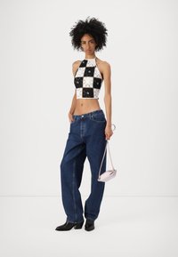 Top corto a scacchi bianco e nero, con collo alto, abbinato a jeans in denim blu larghi e stivaletti neri con tacco. Borsa rosa piccola.