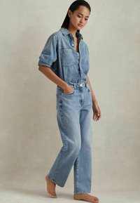 Camisa de denim con botones en el front y bolsillo en el pecho, combinada con jeans rectos de tiro alto en un tono azul claro. Textura suave, corte relajado.