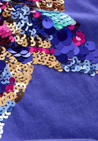Tela morada con una variedad de lentejuelas multicolores en azul, rosa y dorado, que reflejan la luz con una textura suave y brillante.