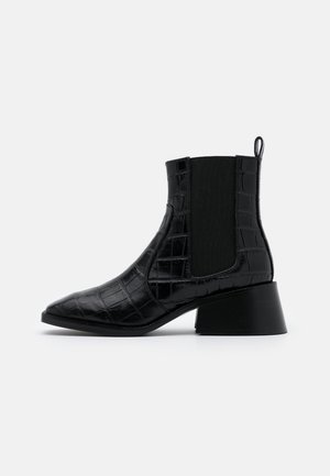 Bottine noire mi-mollet avec bout pointu, talon bloc, texture crocodile, panneaux latéraux élastiques et languette à l'arrière.