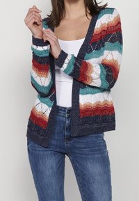Sweter dzianinowy z wielokolorowymi falistymi wzorami w odcieniach czerwieni, turkusu i bieli, z otwartym przodem, długimi rękawami oraz granatowym wykończeniem.