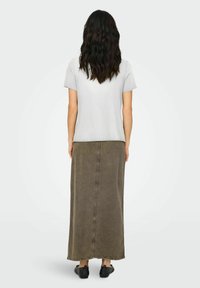Camiseta gris de manga corta combinada con una larga falda de mezclilla verde oliva. La falda presenta una costura central y un dobladillo deshilachado. Zapatos negros sin cordones.