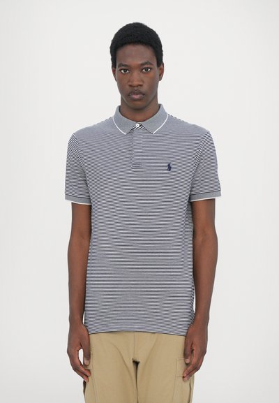 Polo rayé avec une patte de boutonnage à deux boutons, un col et des manches courtes. Les couleurs incluent le bleu marine et le blanc. Logo sur la poitrine gauche. Matériau en coton.