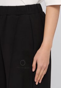 Zwarte broeken met een elastische tailleband, voorzien van plooien en een subtiele Trussardi-logo aan de zijkant, met een soepele textuur en een op maat gemaakt ontwerp.