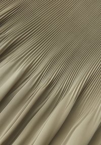 Tessuto beige con sottili pieghe verticali che sfumano in pieghe più morbide, creando un motivo fluido e strutturato.