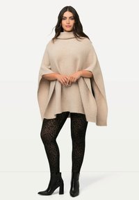 Poncho beige texturizzato con collo a cowl, abbinato a leggings neri con una sottile stampa animalier e stivaletti neri con tacco.
