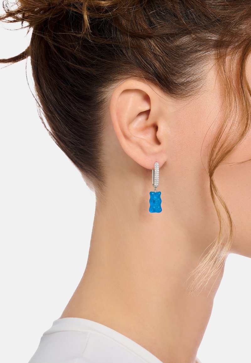 Blauer Gummibären-Ohrring mit silberner Befestigung, bestehend aus einem kleinen runden Stecker und einer hängenden Bärenform mit glänzender Oberfläche.