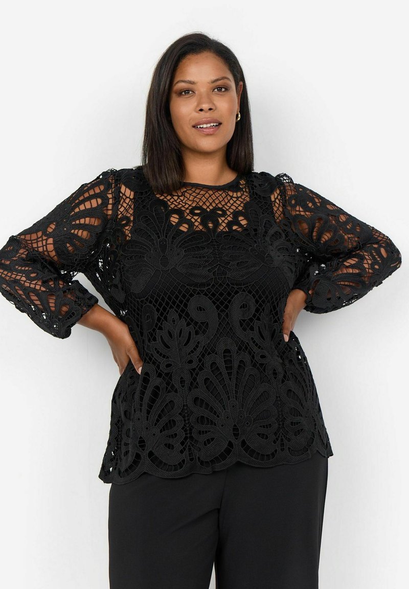 Top in pizzo floreale nero con maniche lunghe, caratterizzato da un orlo a scallop e un design trasparente, sovrapposto a una base in tessuto solido.