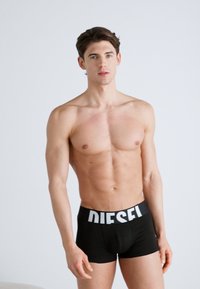 Boxers noirs avec un logo "DIESEL" blanc sur la ceinture. Texture lisse et design ajusté, présentant un style minimaliste et sans couture.