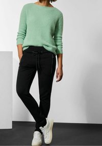 Mintgrön strukturtröja med rundad halsringning, tillsammans med svarta joggers med sidofickor med dragkedja och justerbar dragsko. Vita sneakers.