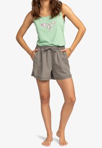 Světle zelený tílko s grafikou srdce, spárované se šedými šortkami na stažení. Tkanina vypadá jemně a má uvolněný střih.