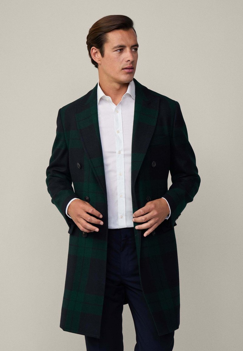 Dvojradový dlhý kabát v tmavozelenej a čiernej kárované vzore, vyrobený z vlny. Má klopové golier, gombíkové detaily a prispôsobený strih.