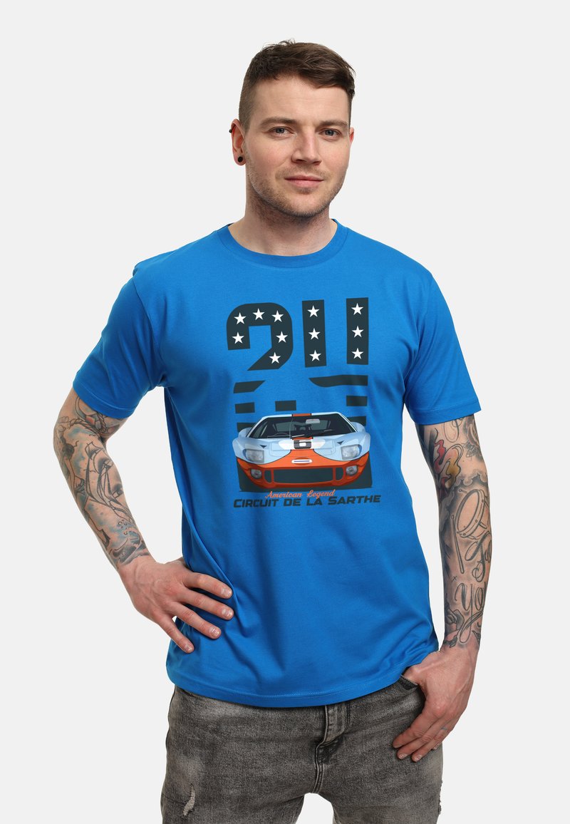 Camiseta azul con un gráfico de un coche de carreras vintage, "24", estrellas y el texto "Circuit de la Sarthe" en colores contrastantes.