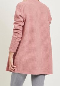 Pitkähihainen vaaleanpunainen neuletakki, joka on valmistettu teksturoidusta kankaasta. Ominaisuuksina rento leikkaus, pyöreä pääntie ja se ulottuu lantion alapuolelle. Ilman kiinnityksiä.