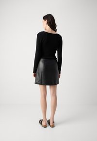 Haut à manches longues noir à côtelés associé à une jupe en cuir noir en forme de A. La jupe présente une texture lisse et un minimum de détails. Des sandales sont portées.